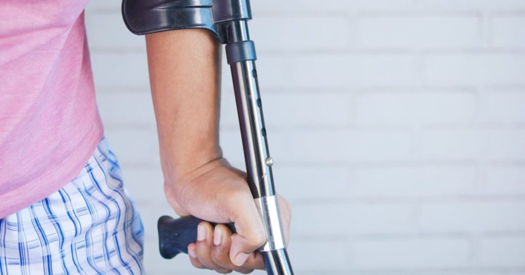 Junge Person stützt sich auf Krücke