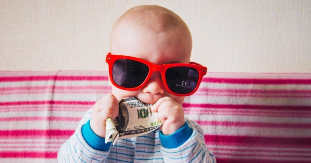 Baby mit Sonnenbrille isst Geldschein